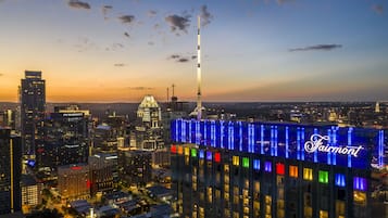 A cityscape at dusk with a prominent building featuring the Fairmont name illuminated in blue.