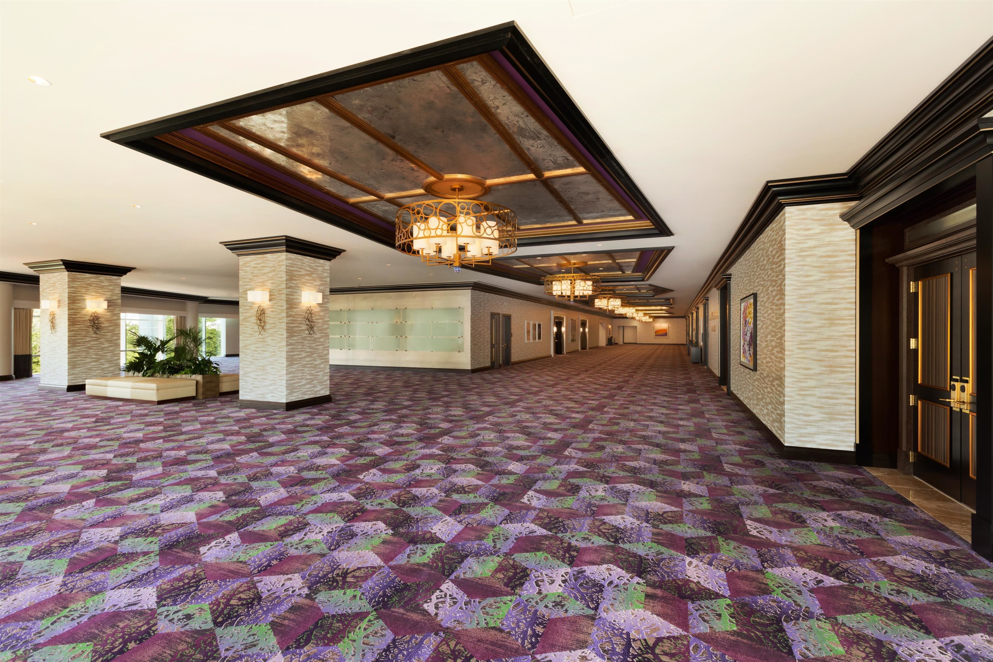 A spacious hallway with patterned carpet, large columns, and a high ceiling with chandeliers.