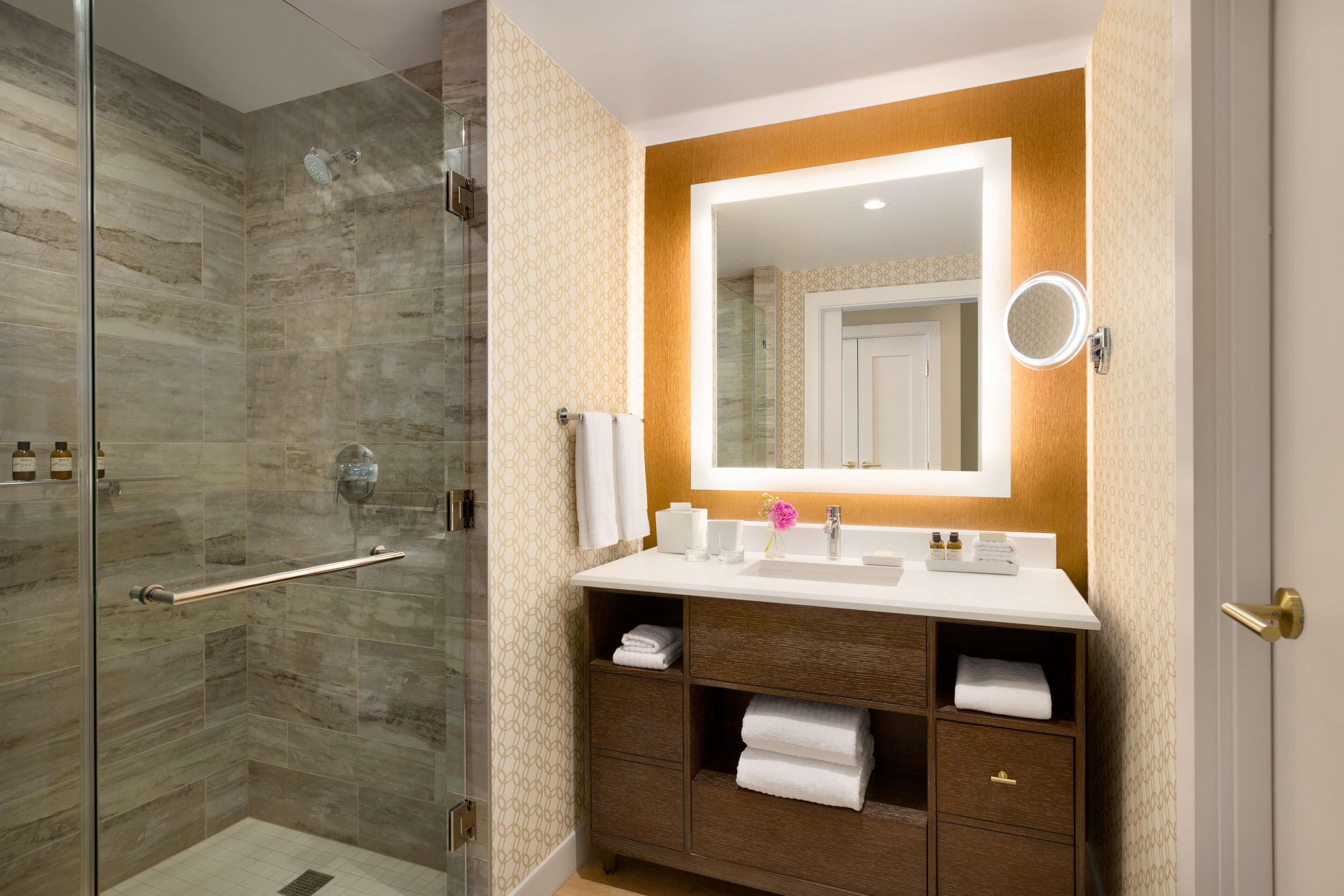 A bathroom with a glass shower enclosure, a vanity with a mirror, and a sink.