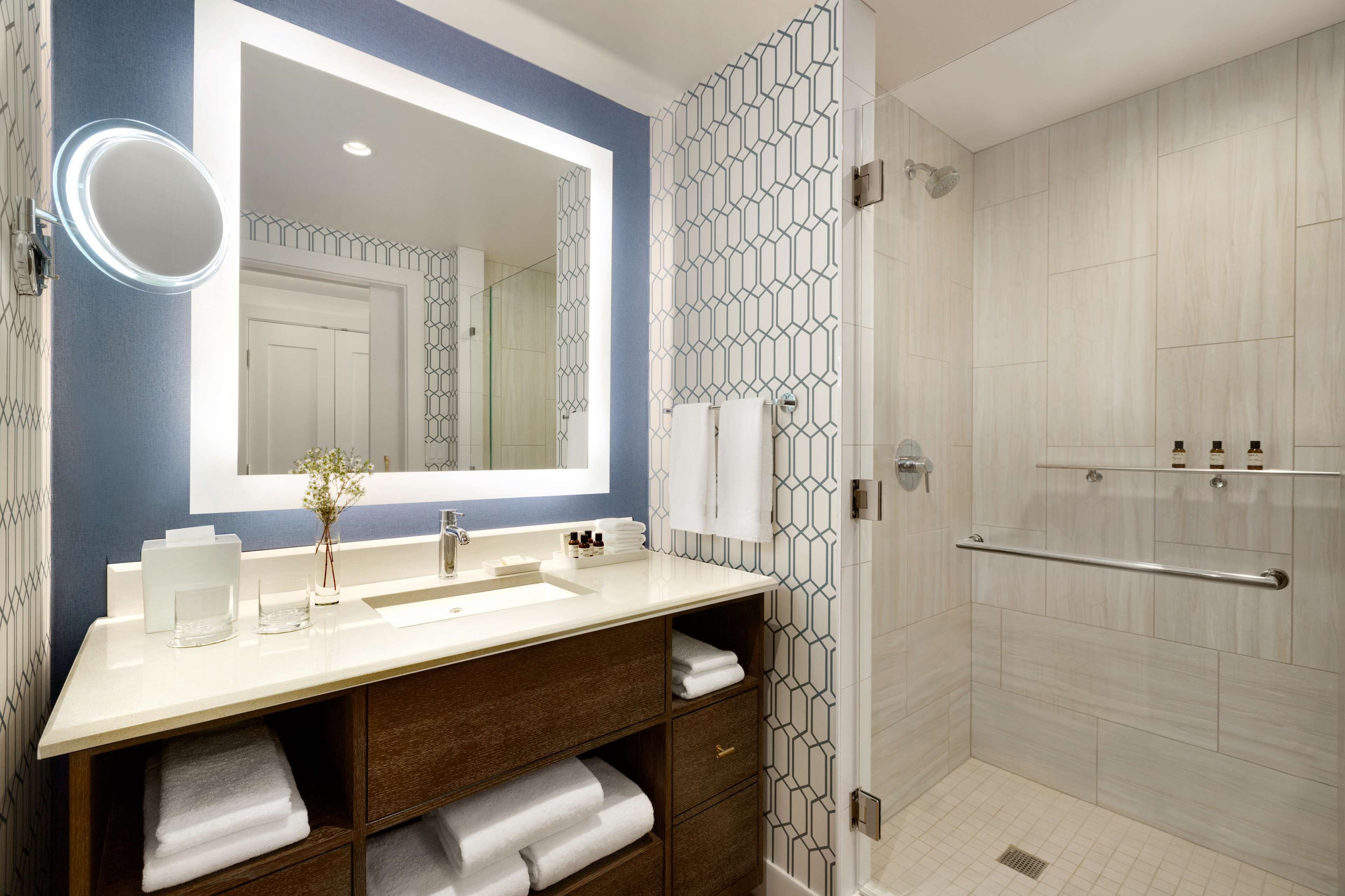 A modern bathroom with a large mirror, a vanity with a sink, and a shower area.