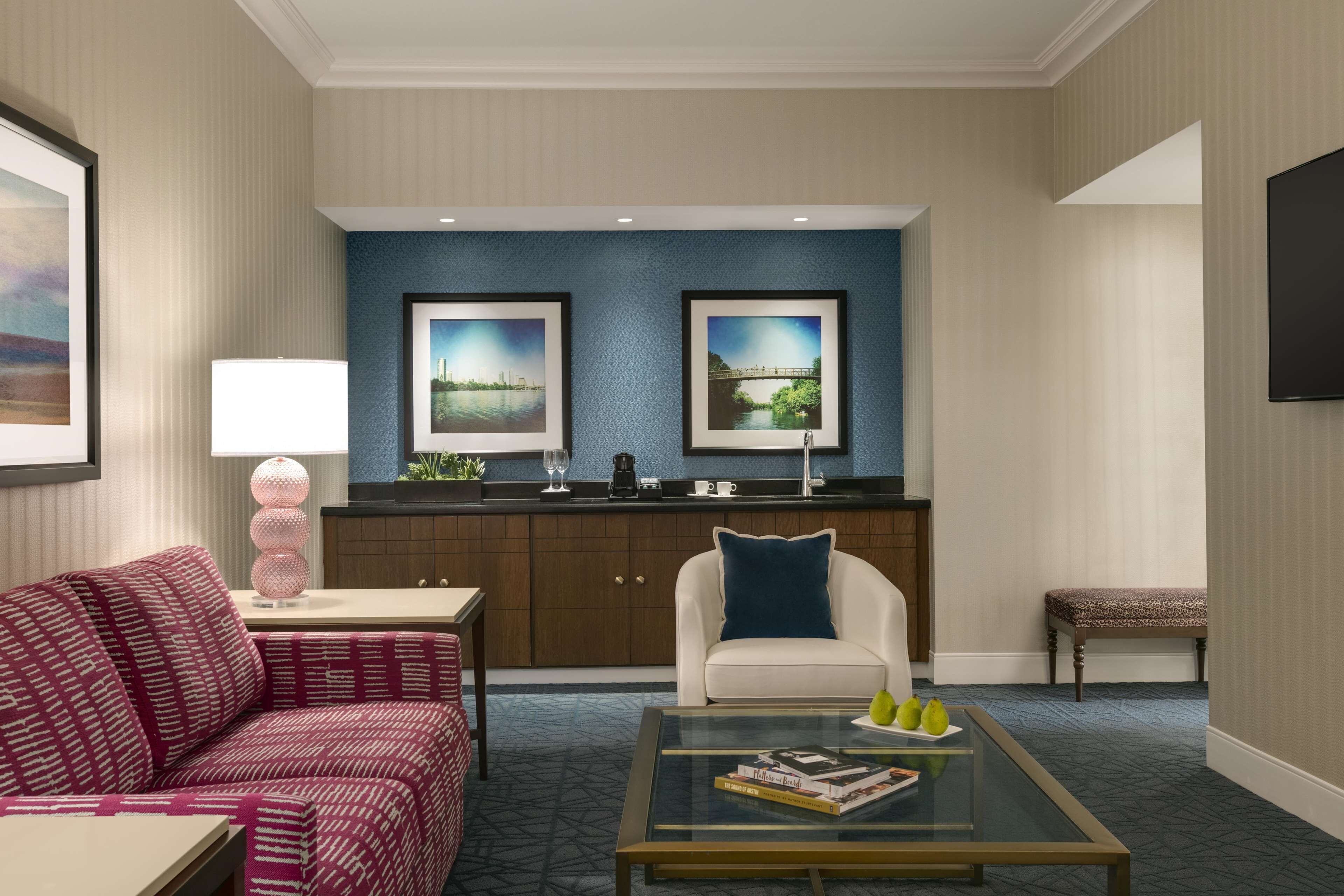 A modern hotel room with a sofa, armchair, coffee table, and a kitchenette area.