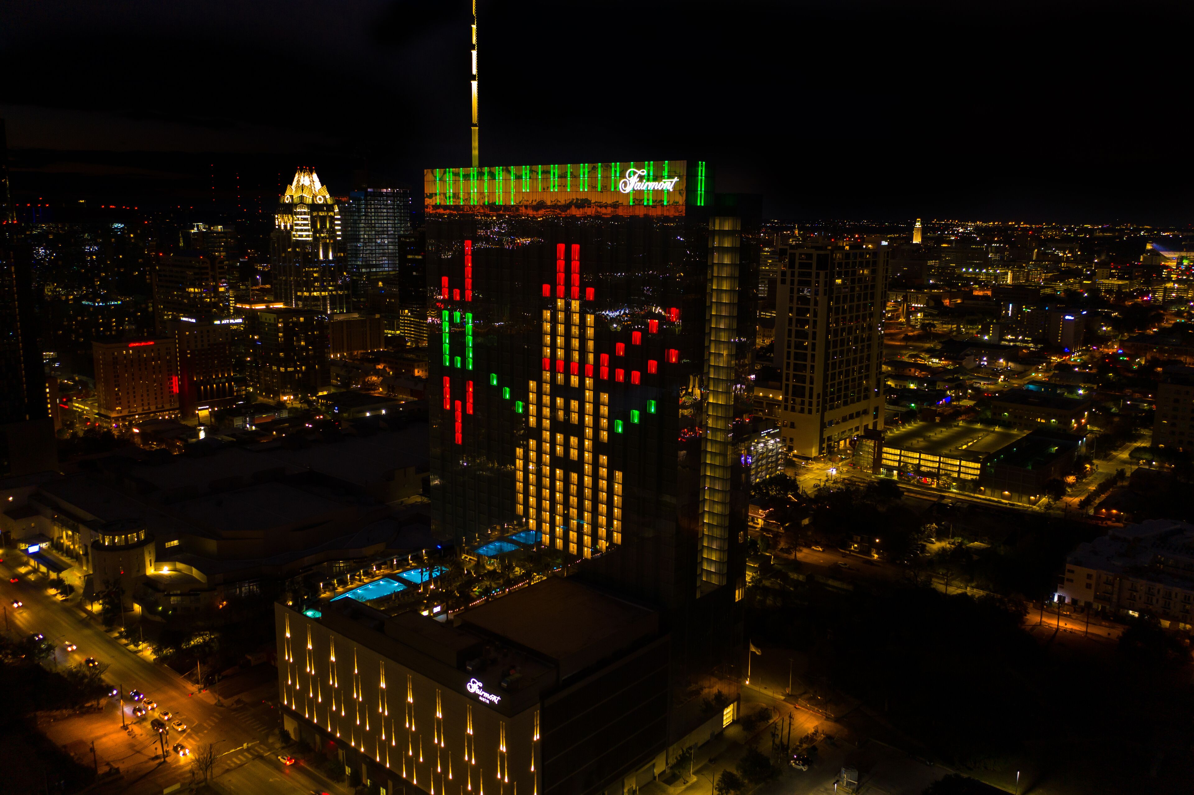 A high-rise building with illuminated vertical bars in red, green, and yellow, and a prominent sign at the top.