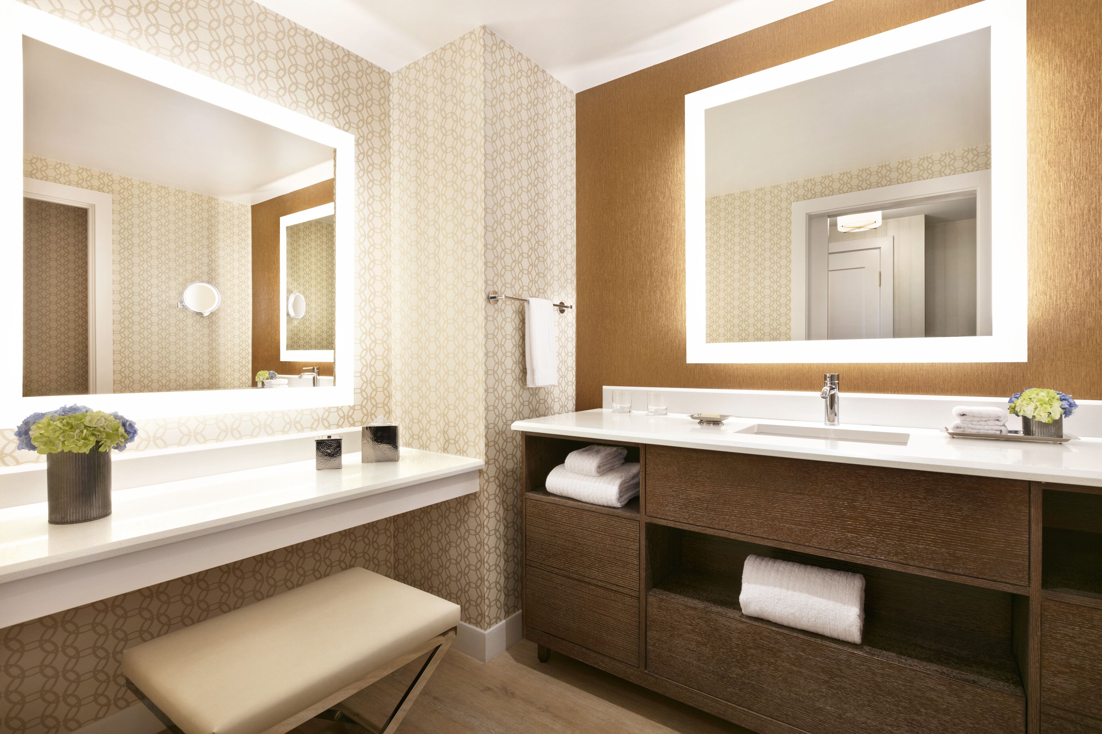 Un baño con dos espejos grandes, un lavabo, un banco y un tocador con estantes.