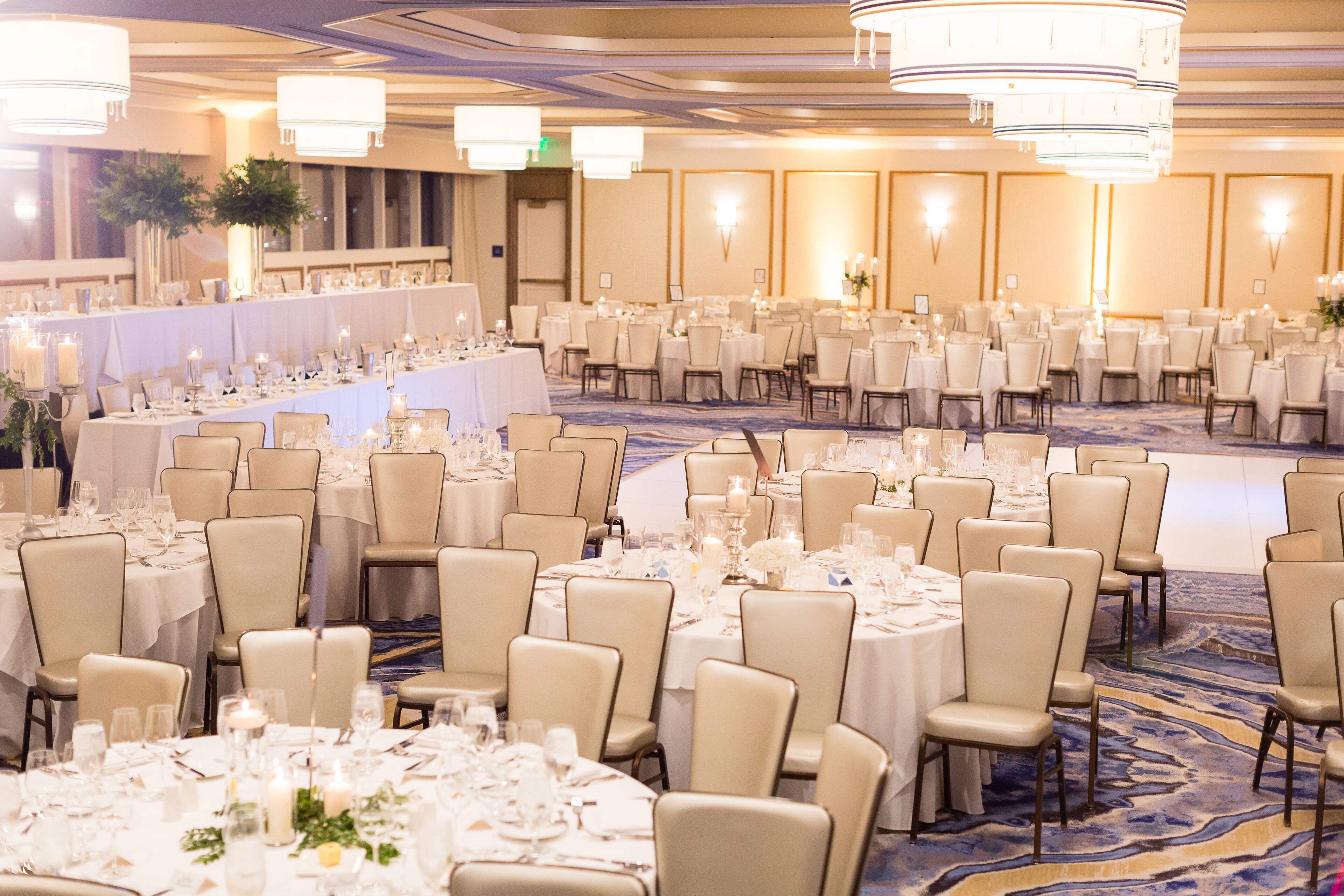 Un salón de banquetes con mesas y sillas redondas, candelabros y centros de mesa florales.