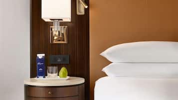 A hotel room with a bedside table, a lamp, a bottle of water, a glass, and a pear.
