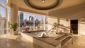 Un espace spa intérieur moderne, doté d’un jacuzzi, de sièges et offrant une vue sur la ville.