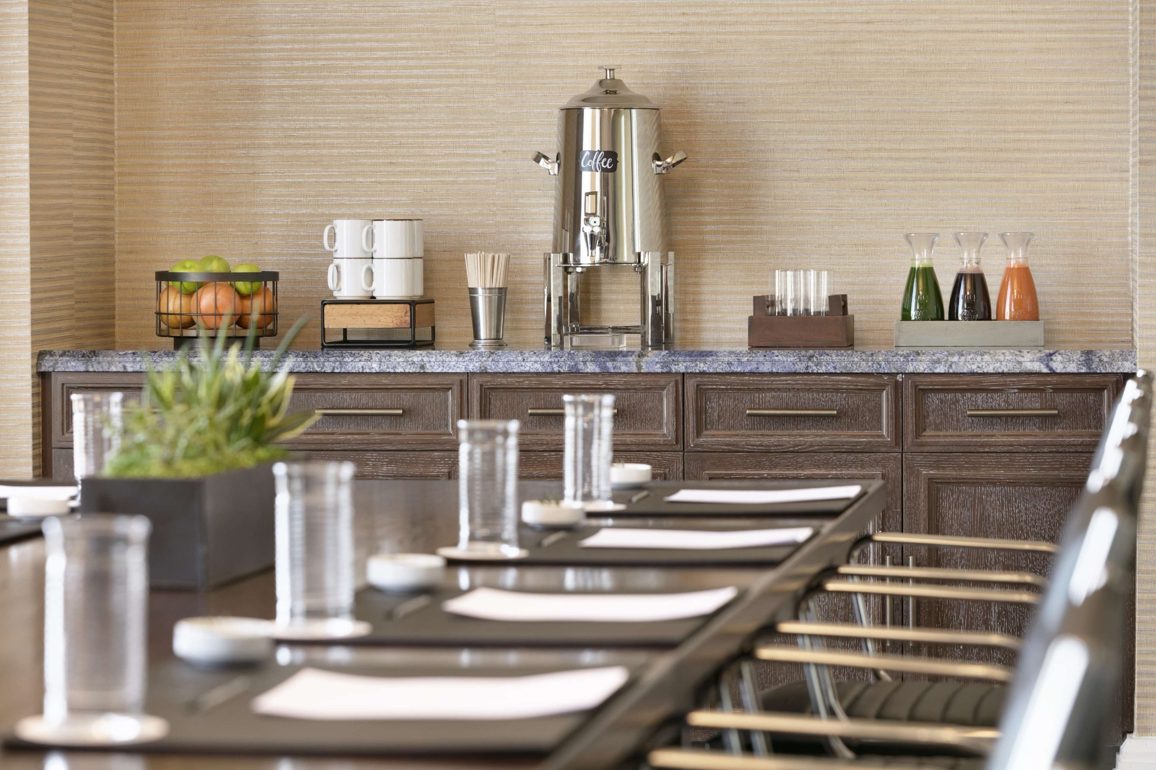 A modern kitchen with a coffee station, a fruit bowl, and a dining area with a long table and chairs.