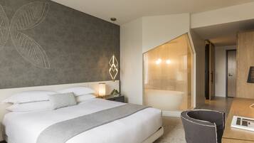 Habitación de hotel moderna con una cama grande, un escritorio y un baño visible a través de una puerta abierta.