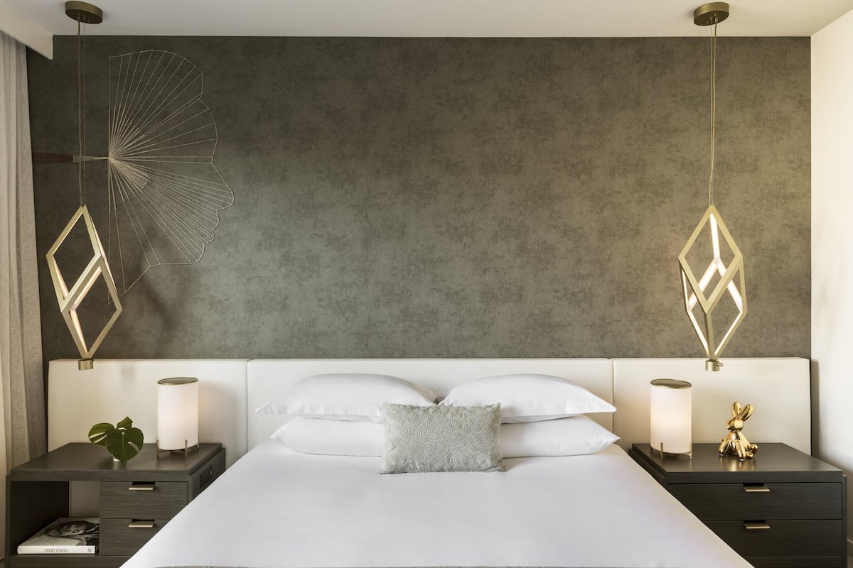 Ein modernes Schlafzimmer mit einem großen Bett, zwei Nachttischen mit Lampen und dekorativer Wandkunst.
