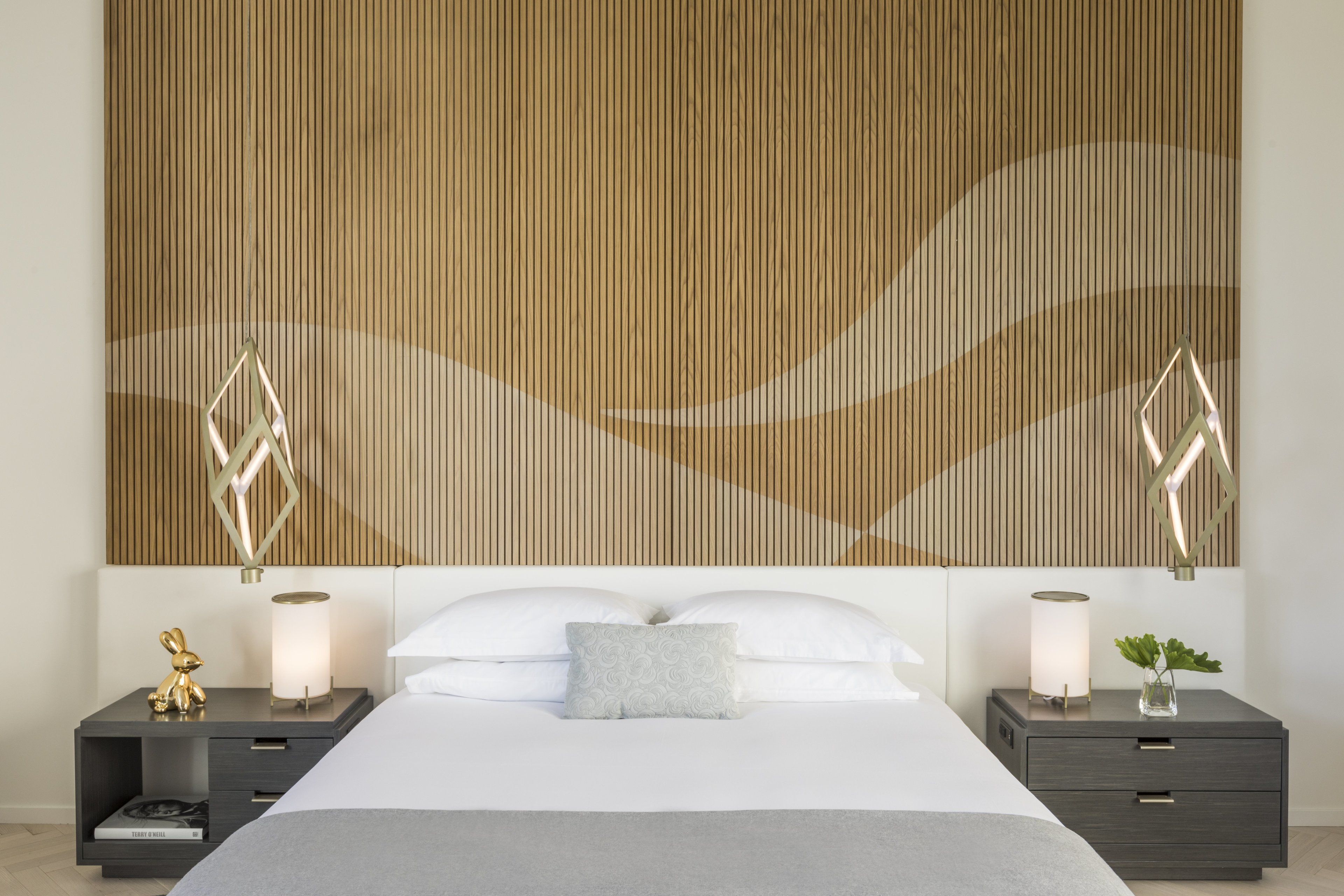 A modern bedroom with a large bed, two bedside tables with lamps, and a decorative wall panel.