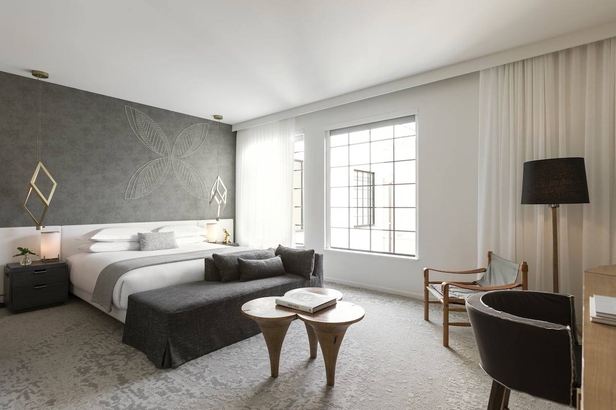 Ein modernes Hotelzimmer mit einem großen Bett, einem Schreibtisch, einem Stuhl, einem kleinen Tisch und einem großen Fenster.