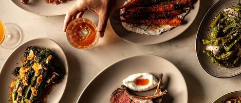 A variety of dishes including roasted meats, vegetables, and a glass of beer on a dining table.