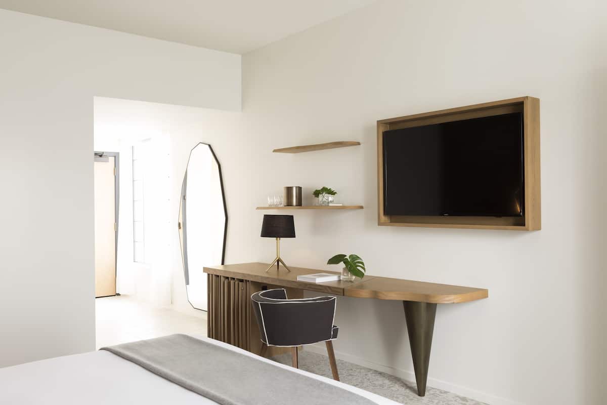 Ein modernes Schlafzimmer mit Schreibtisch aus Holz, einem schwarzen Stuhl, einem Nachttisch und einem großen Spiegel.