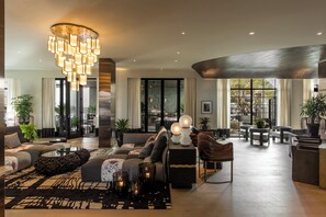 A spacious living area with a modern chandelier, comfortable seating, and a view through large windows. - Kimpton La Peer West Hollywood (West Hollywood)