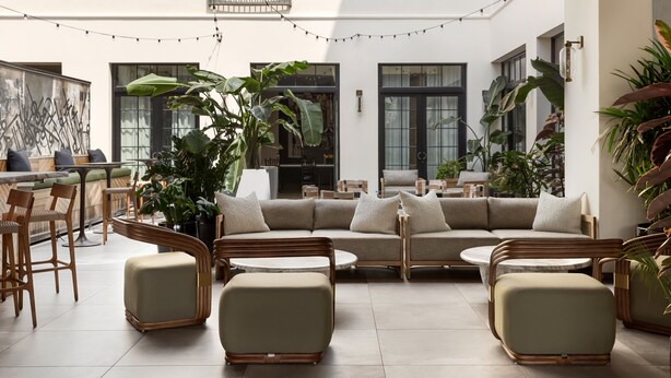 A spacious indoor area with a large sofa, round tables, and chairs. There are potted plants and a string of lights.