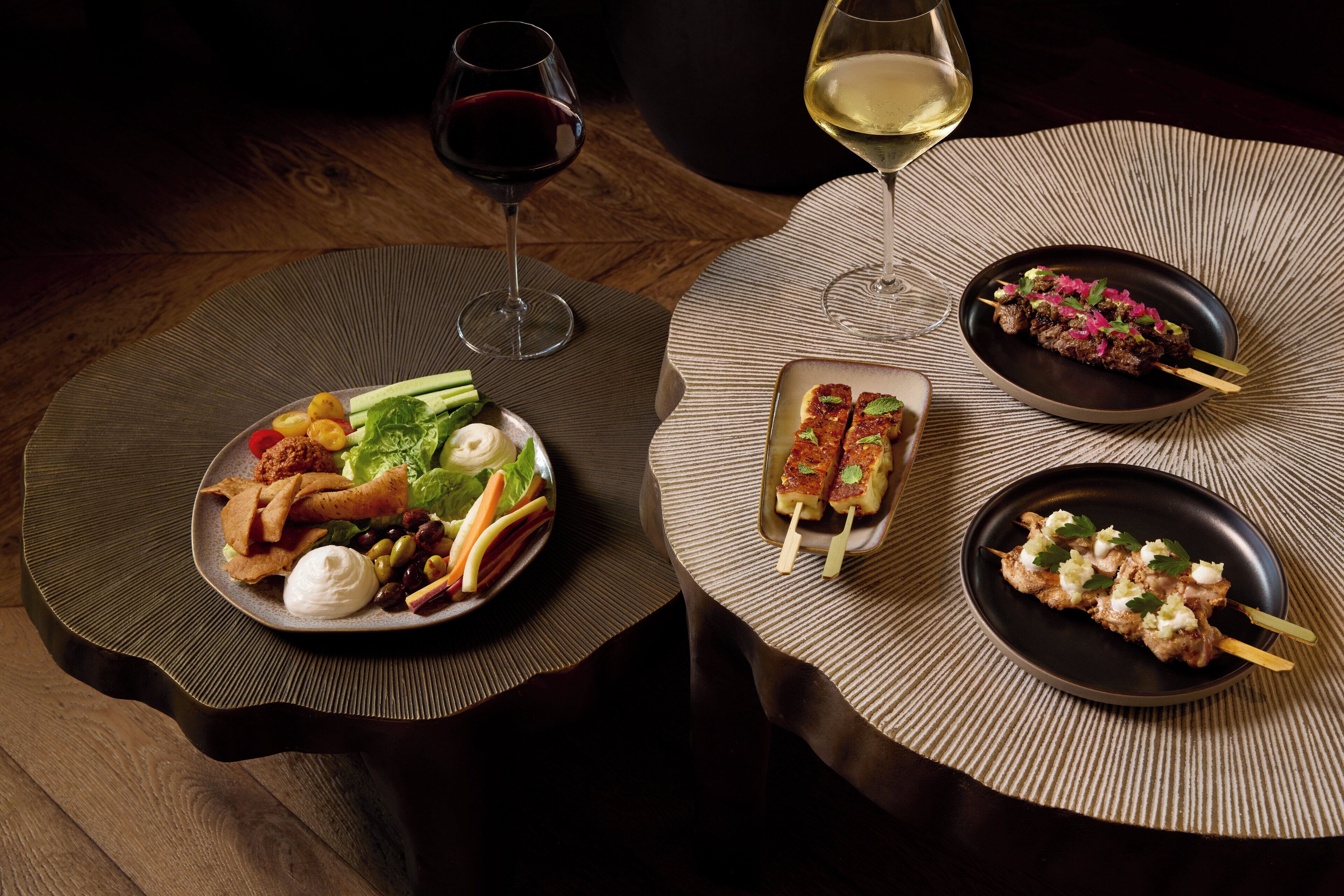 A dining table with plates of food, two glasses of wine, and a textured placemat.