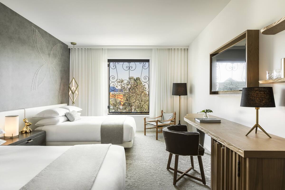 Ein Hotelzimmer mit zwei Betten, einem Schreibtisch, einem Stuhl, einer Lampe und einem großen Fenster mit Blick.