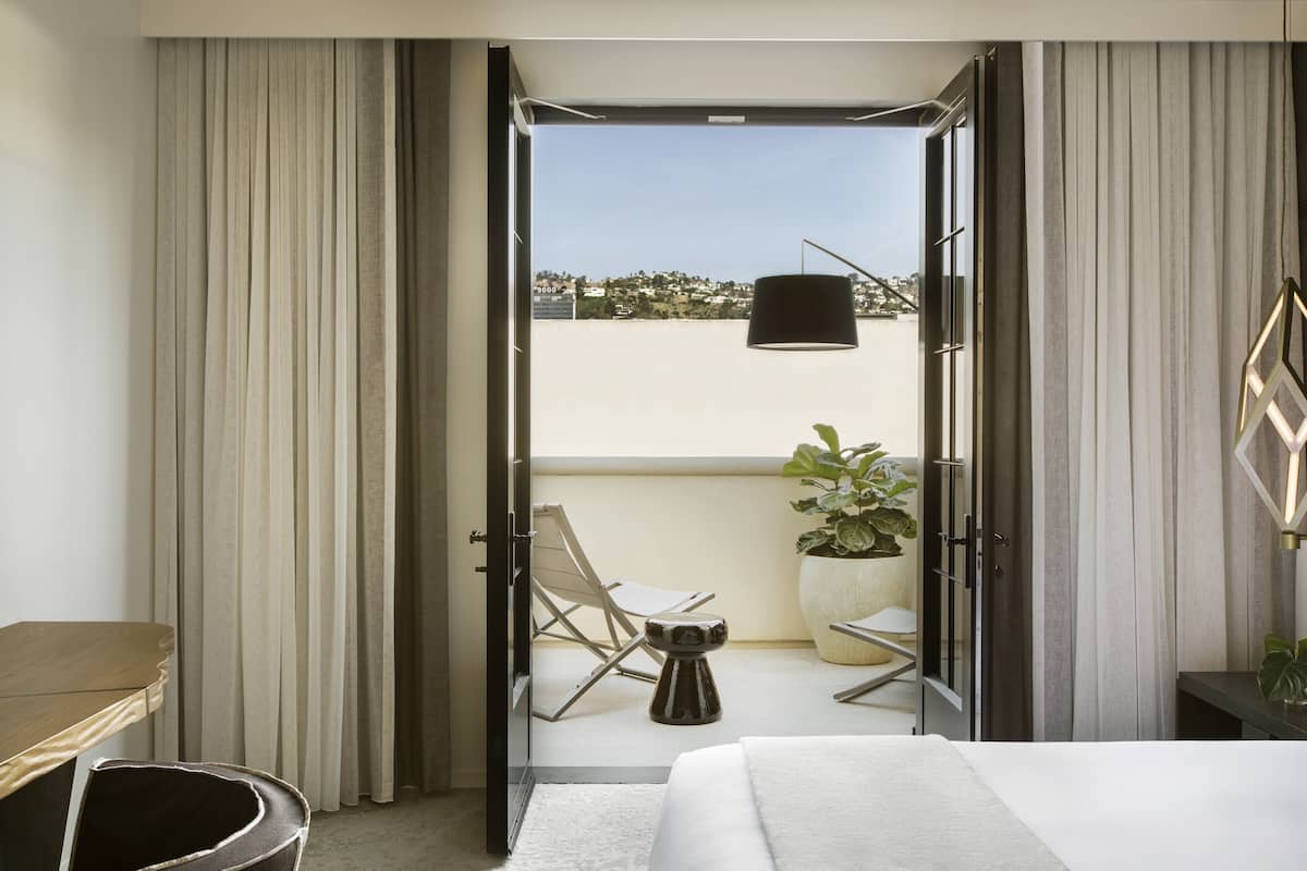 Ein Hotelzimmer mit Balkon, einem Bett, einem Sessel und einer Topfpflanze.