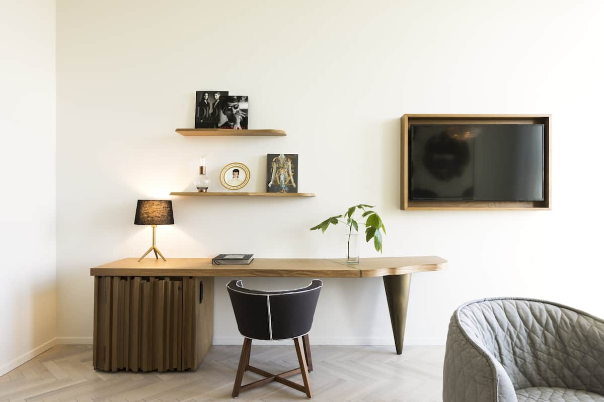 Ein moderner Arbeitsplatz mit einem Holztisch, einem schwarzen Stuhl, einem kleinen Hocker und Regalen mit Dekorationselementen.