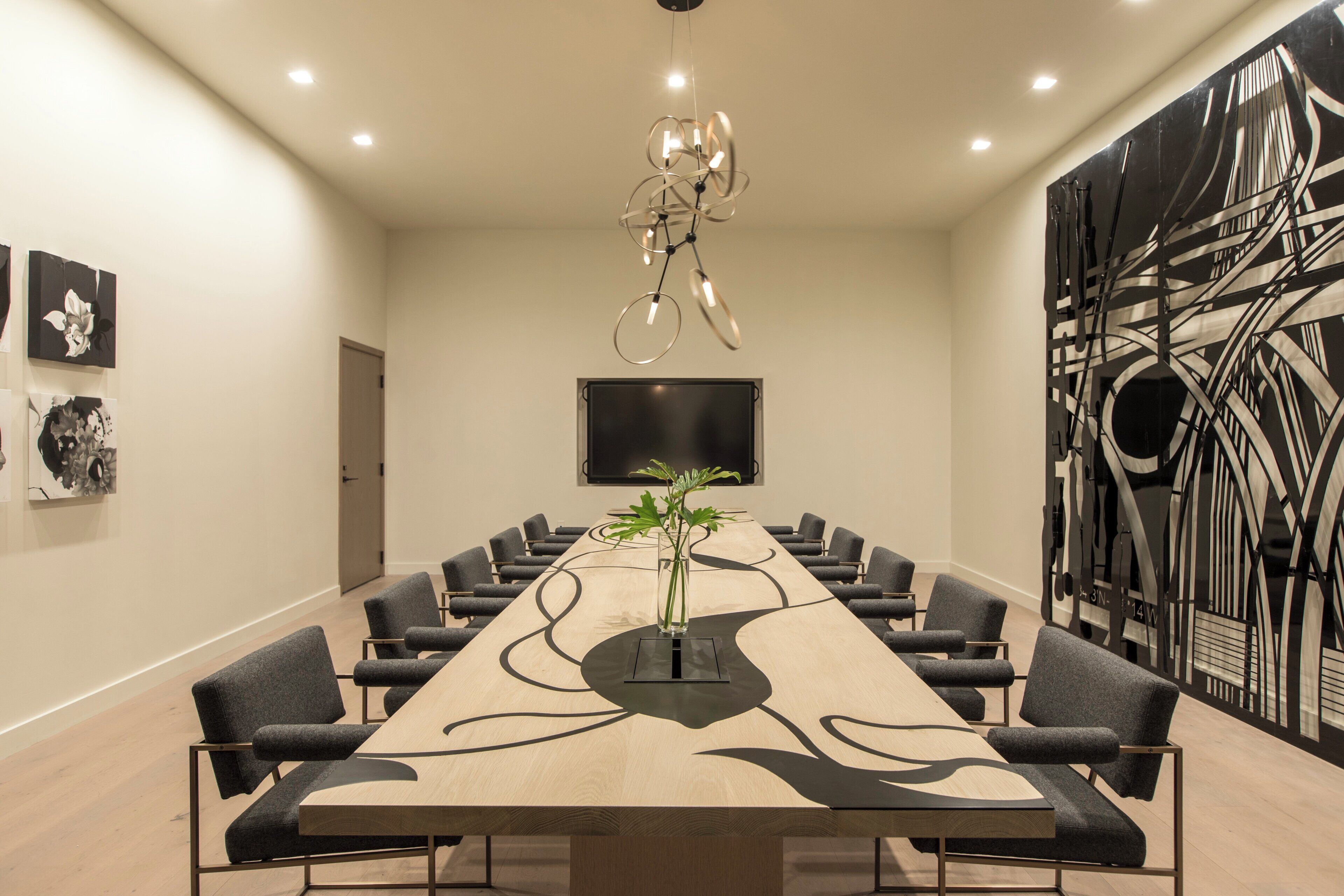 A conference room with a long table, chairs, a plant, and a modern abstract wall art piece.
