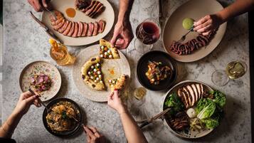 A group of people dining at a table with various dishes, including pizza and meat, and wine glasses.