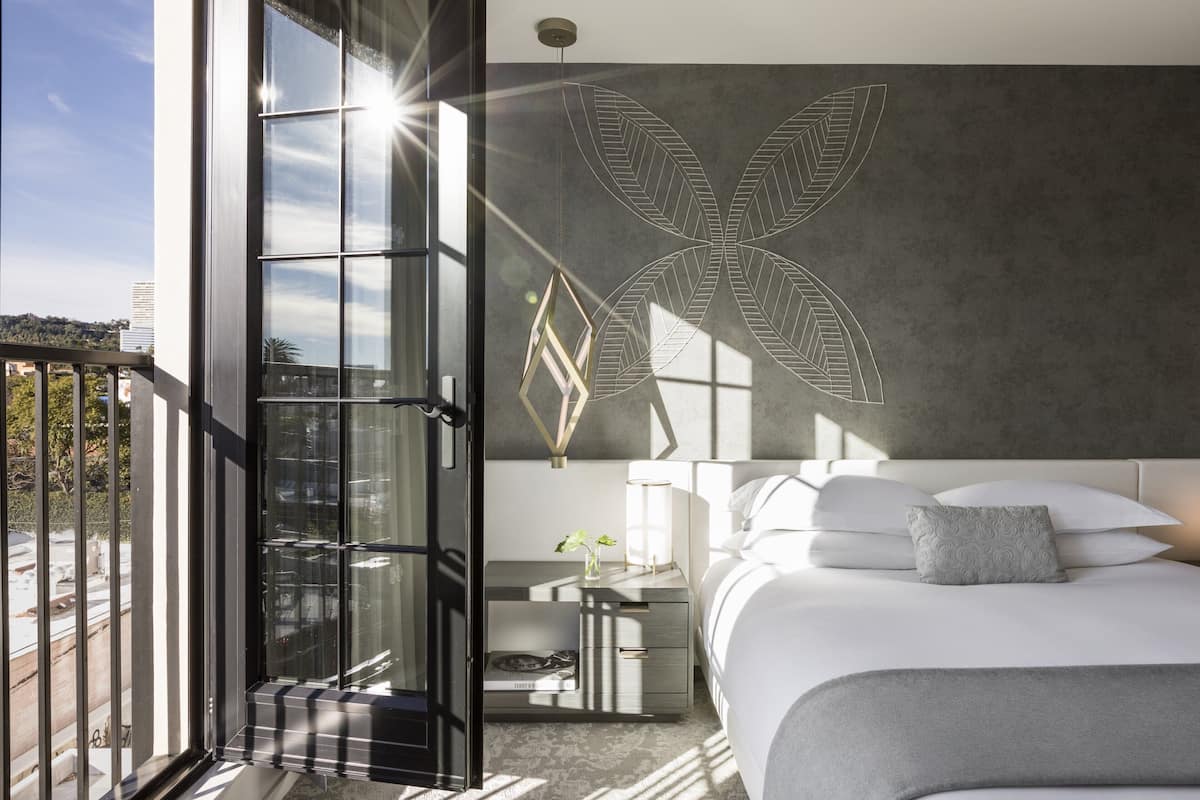 Ein modernes Hotelzimmer mit einem großen Bett, einem Nachttisch, einer Wandleuchte und einem Balkon mit Blick auf die Stadt.