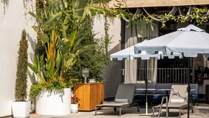 A poolside area with lounge chairs, a wooden cabinet, and a large umbrella.