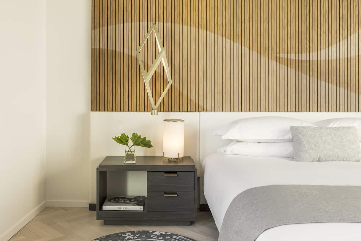 Ein modernes Schlafzimmer mit Bett, Nachttisch, Lampe und einer dekorativen Wandverkleidung.