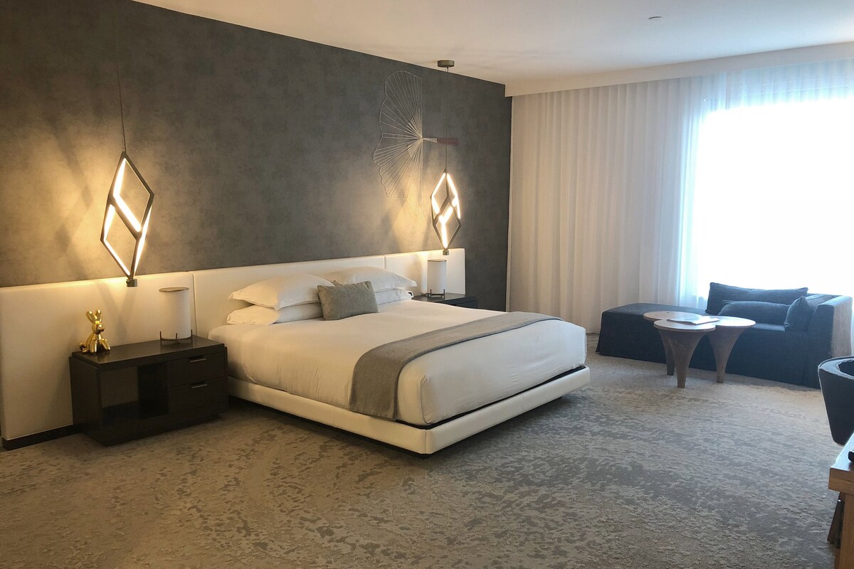 A modern hotel room with a large bed, bedside tables, a small round table, and a sofa.