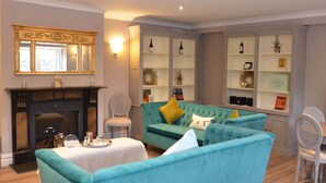 A living room with a fireplace, teal sofas, and a bookshelf with decorative items. - The Lawrence (Athboy)