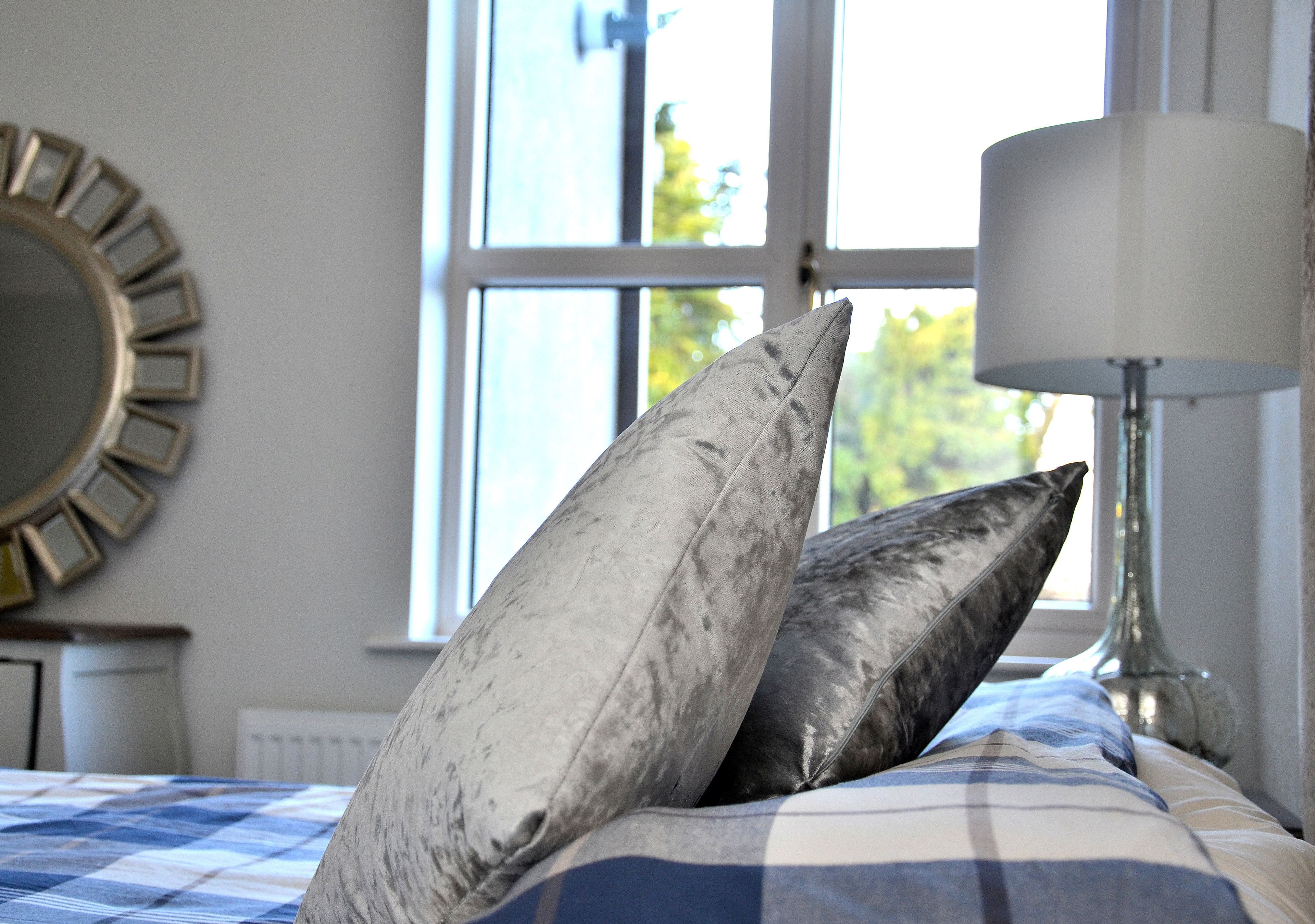 A bed with a checkered bedspread, two pillows, a lamp, and a window with a view of trees.