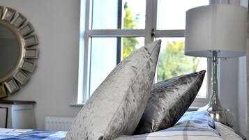 A bed with a checkered bedspread, two pillows, a lamp, and a window with a view of trees.
