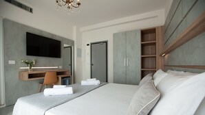 A modern hotel room with a large bed, a desk with a chair, a flat-screen TV mounted on the wall, and a wardrobe with multiple shelves. - Hotel Maestri (Riccione)
