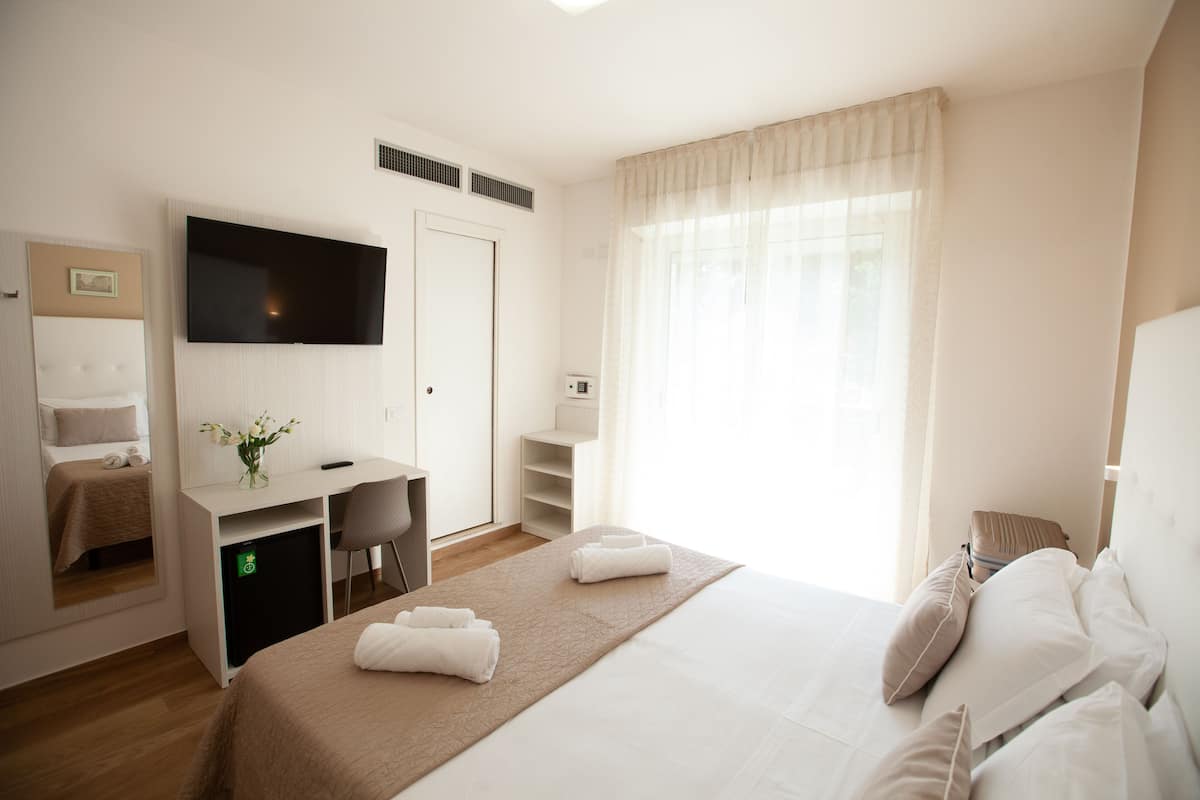 A hotel room with a bed, a desk, a chair, a television, and a window with curtains.