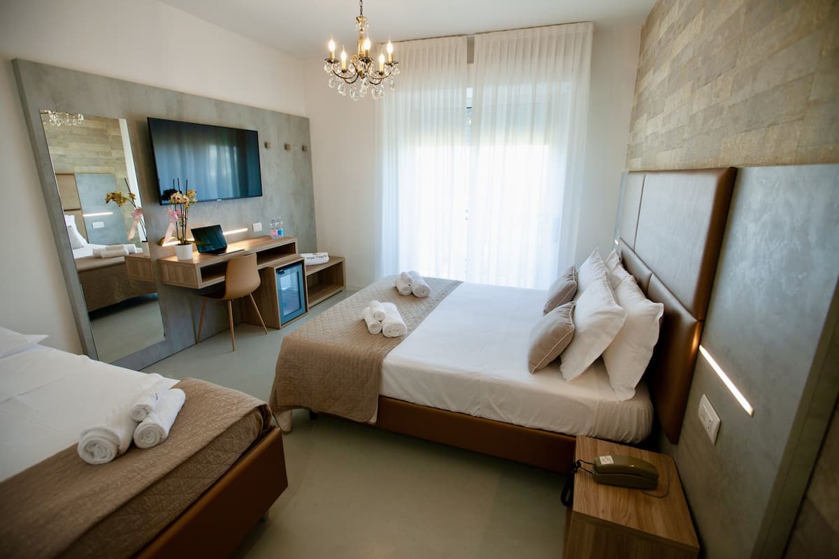 A hotel room with two beds, a desk, a TV, and a chandelier.