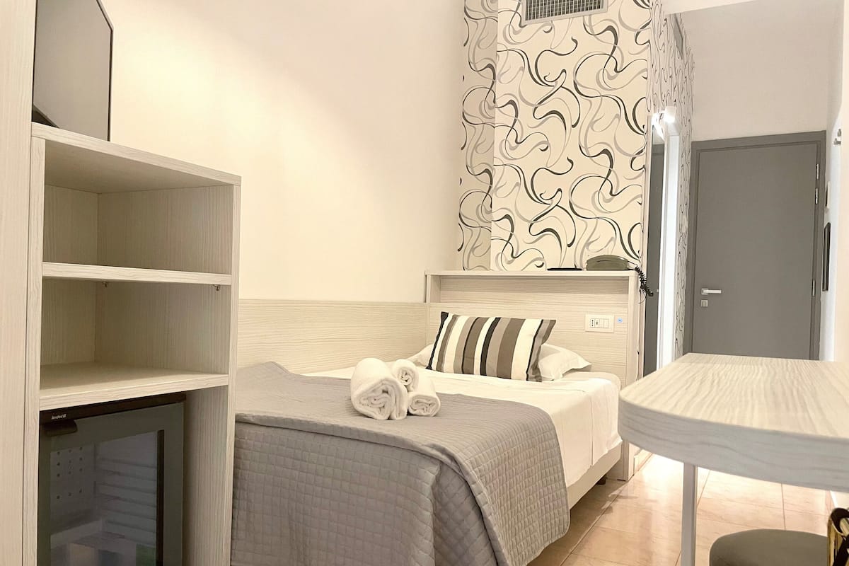 A hotel room with a bed, a bedside table, a chair, a wardrobe, and a door.