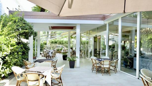 An outdoor patio with wicker furniture, glass doors, and potted plants. - Hotel Maestri (Riccione)
