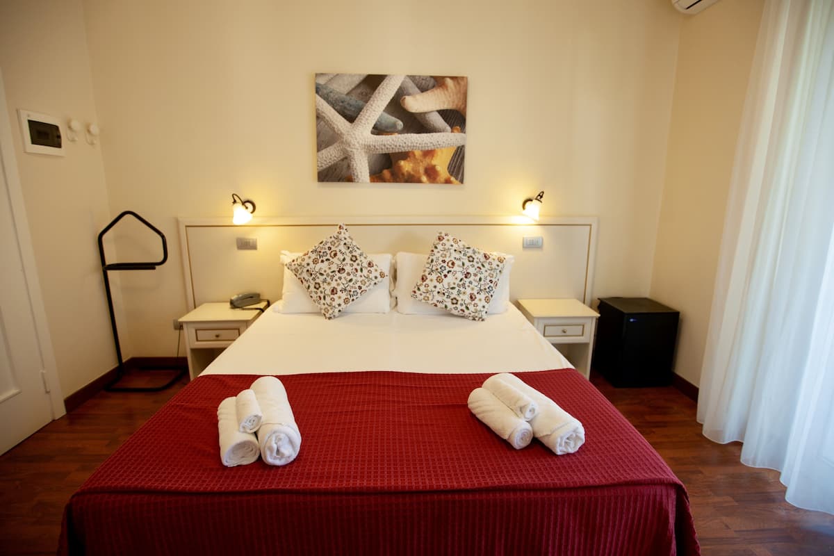 A hotel room with a large bed, two nightstands, a wall-mounted artwork, and a red bedspread.