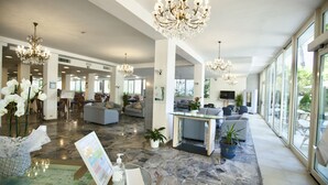 A spacious hotel lobby with marble flooring, modern chandeliers, and large windows offering views of the outdoors. - Hotel Maestri (Riccione)