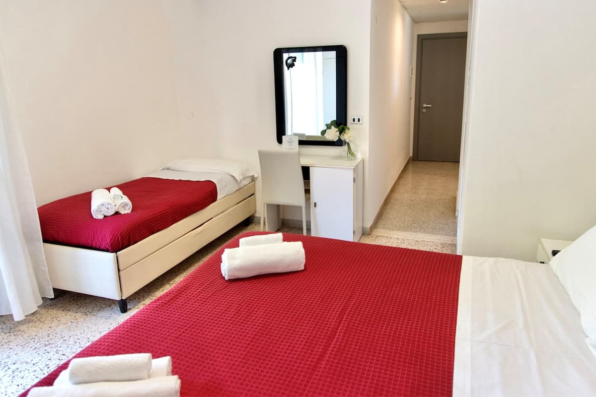A hotel room with a single bed, a desk, a mirror, and a small cabinet.