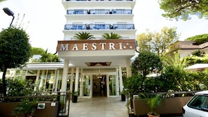 A multi-story hotel named MAESTRI with a modern design, featuring balconies on each floor and a well-maintained garden area in front. - Hotel Maestri (Riccione)