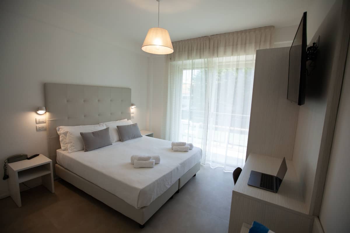 A modern hotel room with a large bed, bedside lamps, a desk with a laptop, and a TV mounted on the wall.