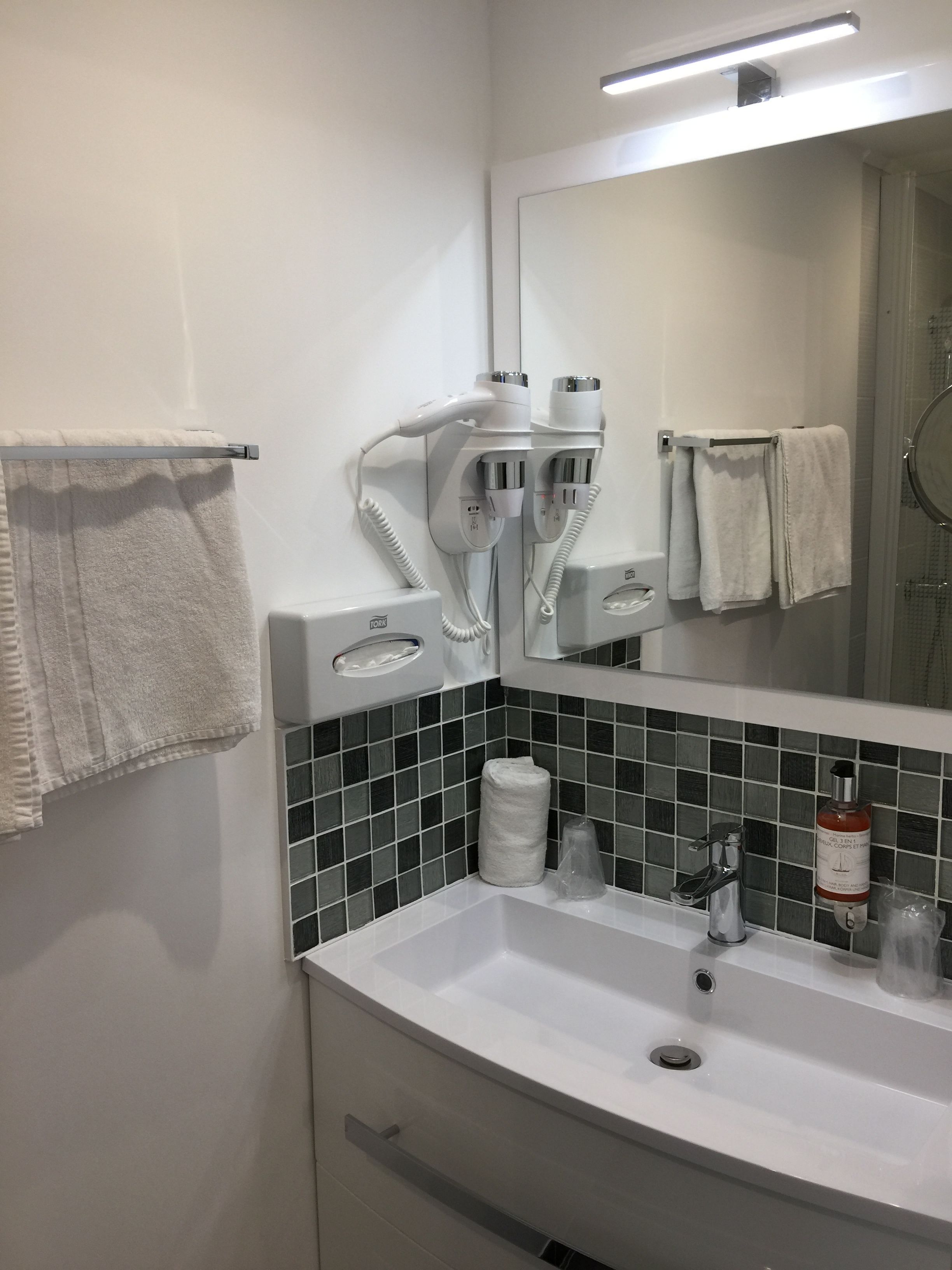 Un baño con lavamanos blanco, espejo, toallero y secador de pelo.