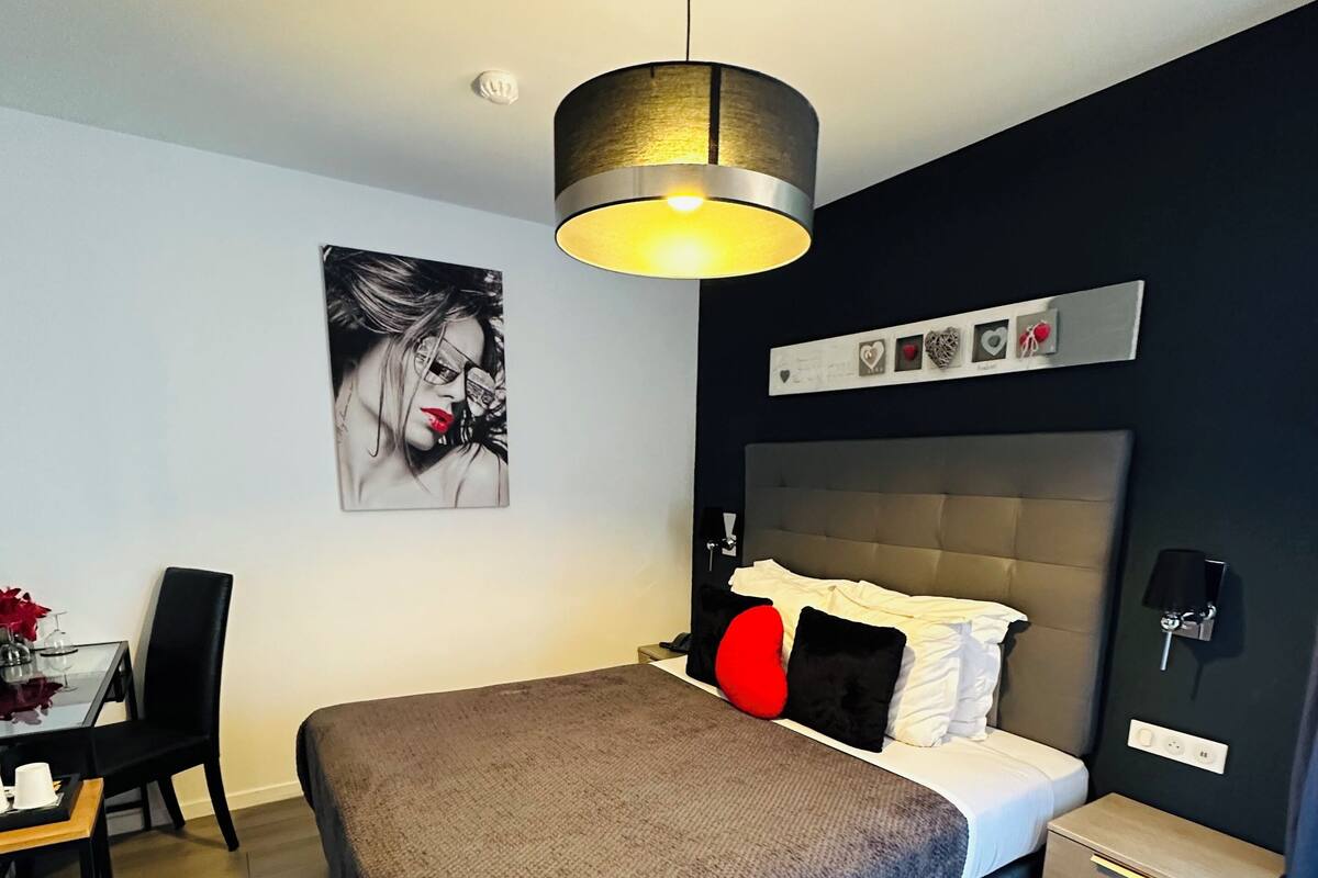 A modern bedroom with a large bed, a desk with a chair, and a hanging light fixture.