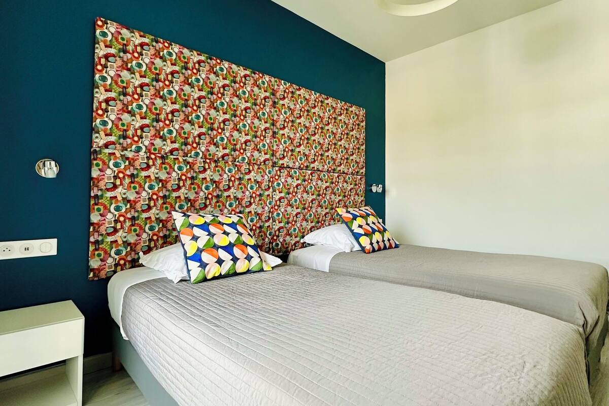 A bedroom with a large bed, two bedside tables, a colorful headboard, and a modern ceiling light.