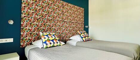 A bedroom with a large bed, two bedside tables, a colorful headboard, and a modern ceiling light.