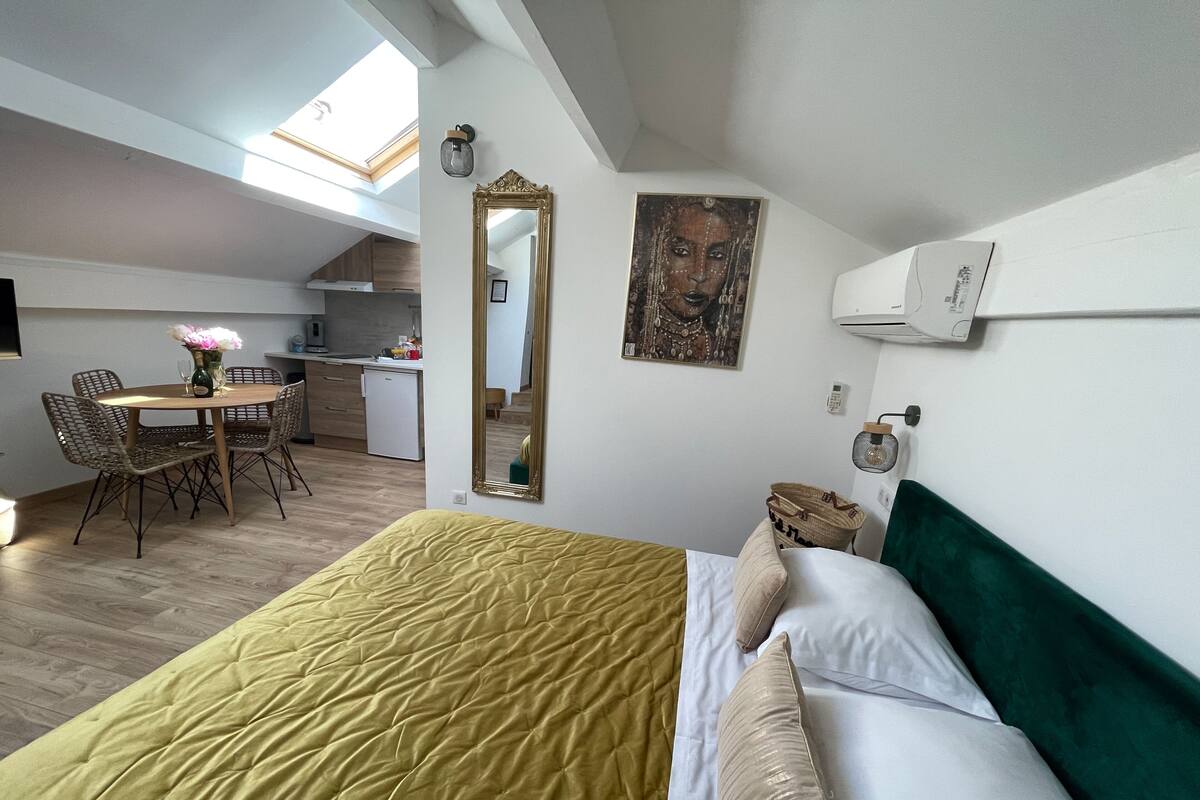 A compact room with a bed, a dining table, chairs, a mirror, and a painting.