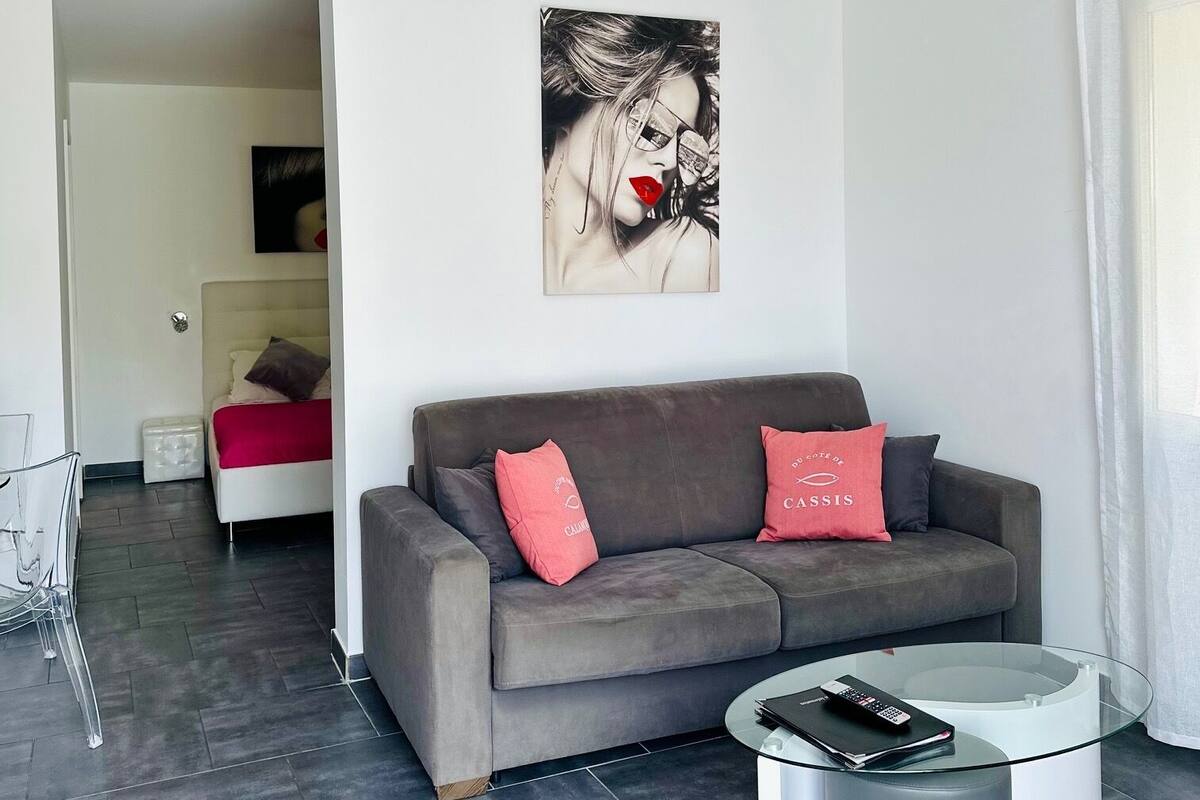 A modern living room with a grey sofa, two red cushions, a glass coffee table, and a framed artwork on the wall.