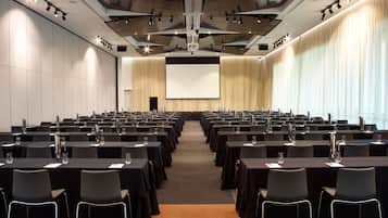 A conference room with rows of tables and chairs, a large screen, and a projector.