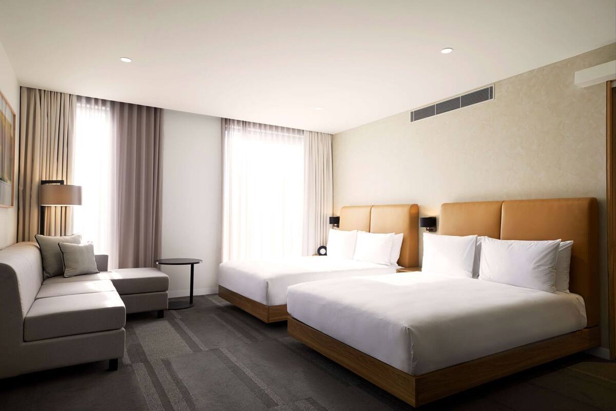 A hotel room with two beds, a sofa, a small table, and a lamp.